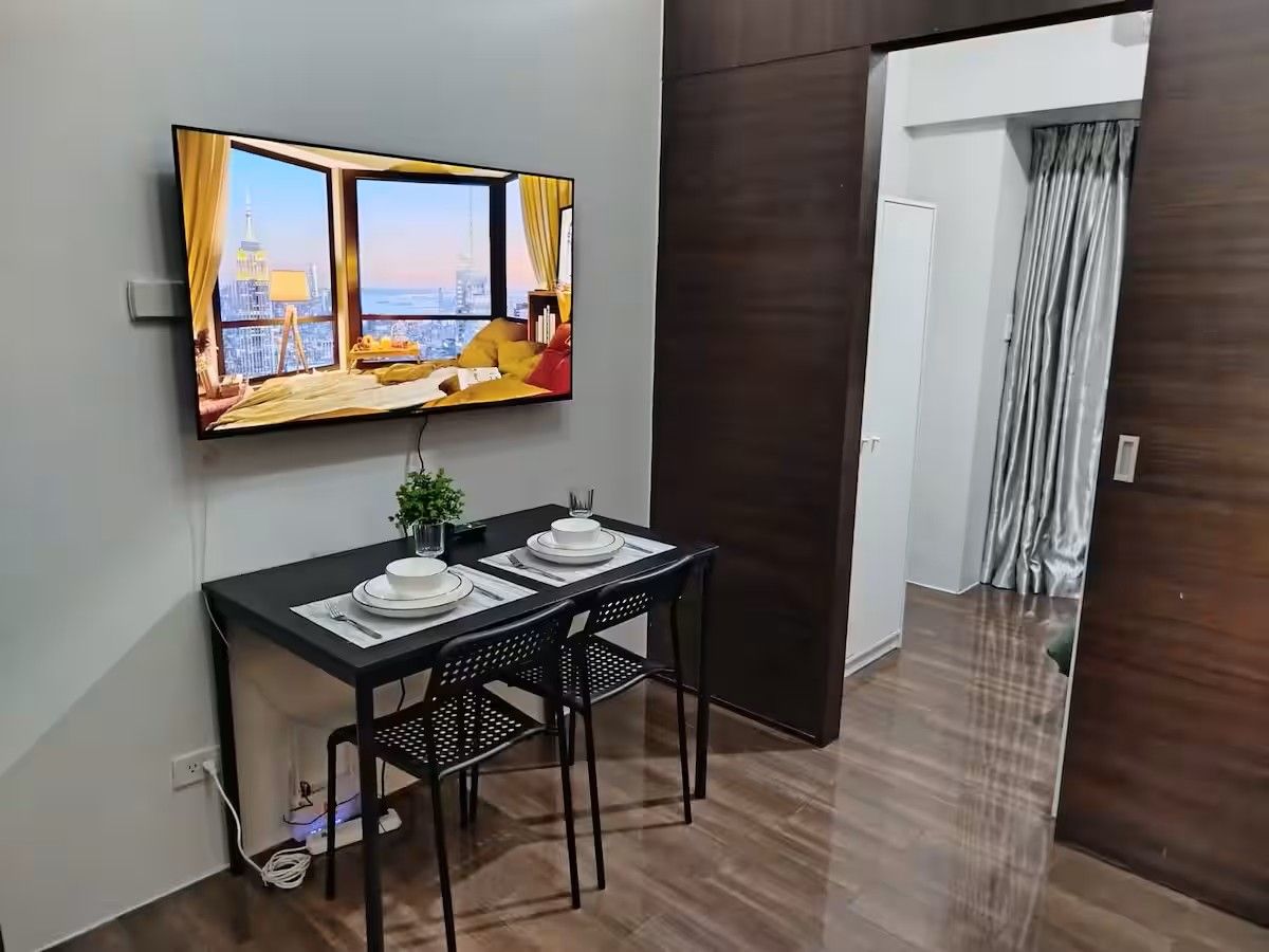 A modern room with a dining table, chairs, a TV mounted on the wall, and a view of a cityscape.