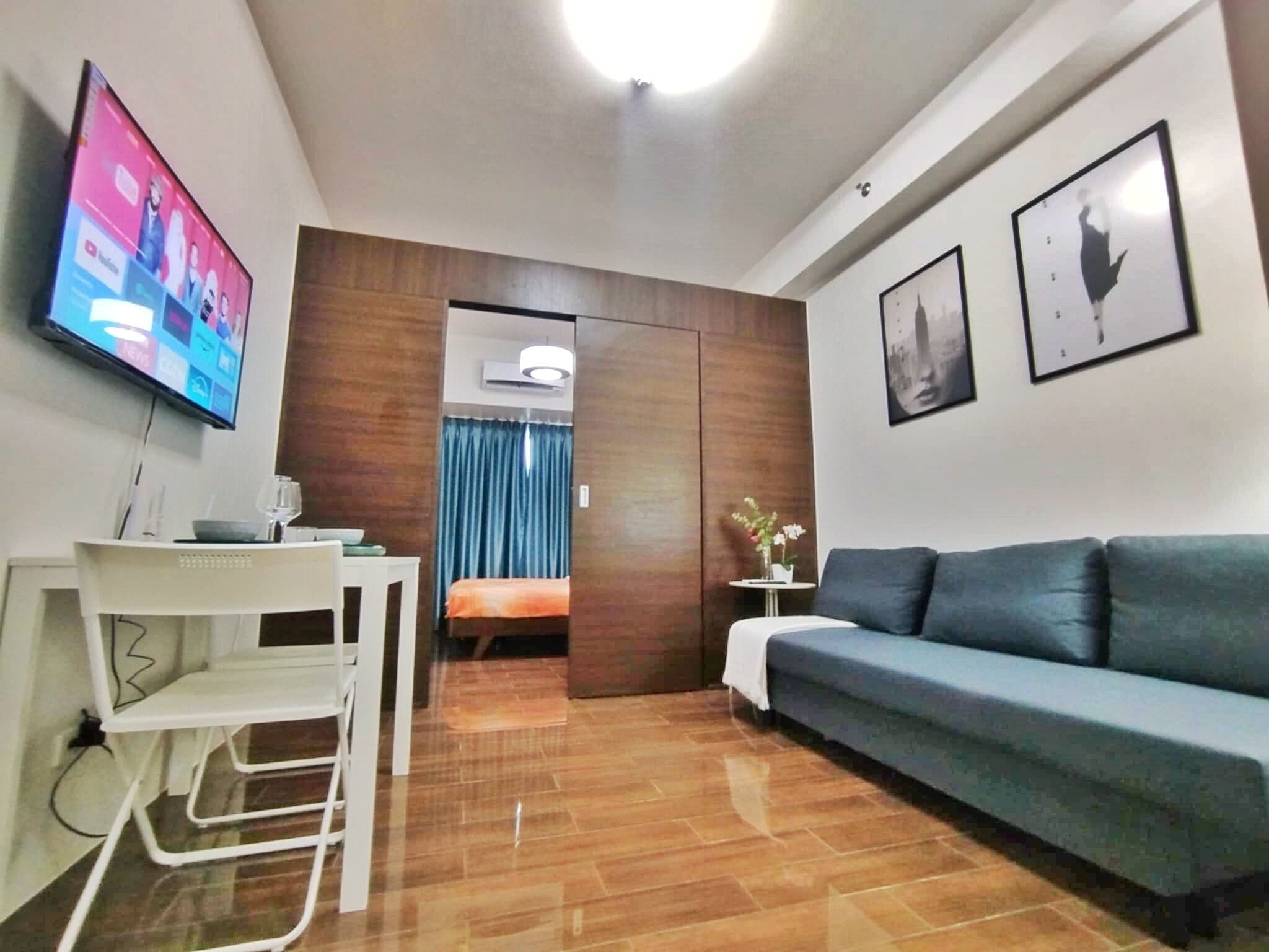 Une chambre d’hôtel moderne avec un canapé bleu, un téléviseur fixé au mur et une cloison en bois.