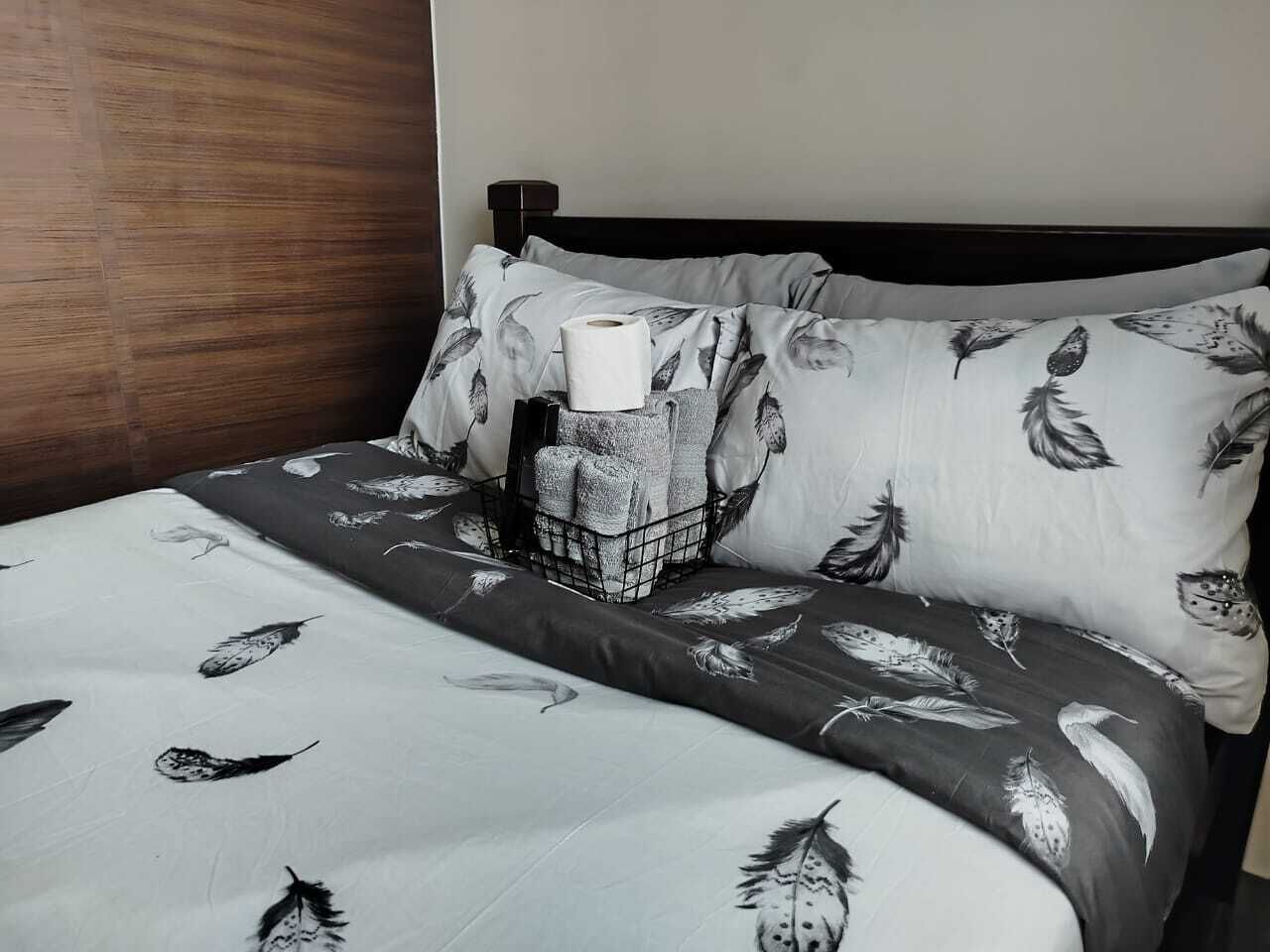 Un lit avec une couvre-lit à motifs et des oreillers, une table de chevet avec une boîte de mouchoirs et une tête de lit en bois.