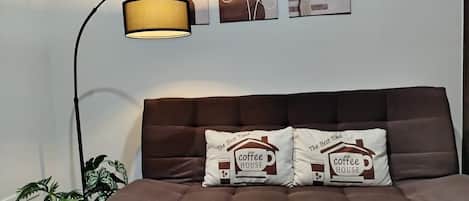 A brown sofa with two decorative pillows, a floor lamp, and wall art.