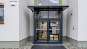 A building entrance with a glass door, a sign with the number 44, and a small outdoor area with gravel. - Apartments Deluxe Barcelona 55 (Kraków)