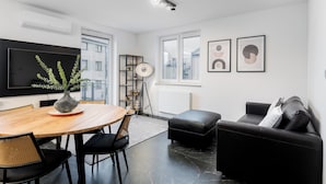 Ein modernes Wohnzimmer mit Holzesstisch, schwarzer Ledersofa und einem flachbildfernseher an der Wand.