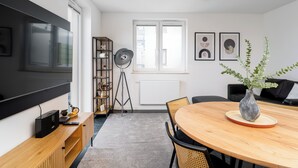 Ein modernes Wohnzimmer mit einem großen Flachbildfernseher, einem Holzessttisch und einem schwarzen Sofa.
