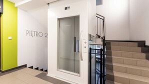 Ein moderner Aufzug mit Glastür, eine Treppe mit Metallgeländern und ein Schild, das einen barrierefreien Bereich kennzeichnet.
