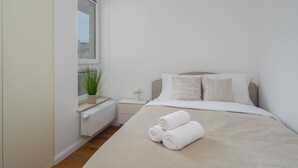 Ein Schlafzimmer mit Bett, Kissen, Heizkörper, Fenster und einer Pflanze.