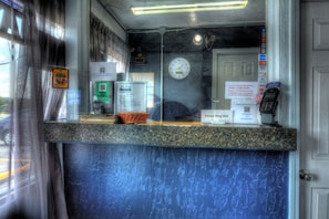 Un comptoir d’accueil d’hôtel avec une horloge, un téléphone et divers panneaux d’information.