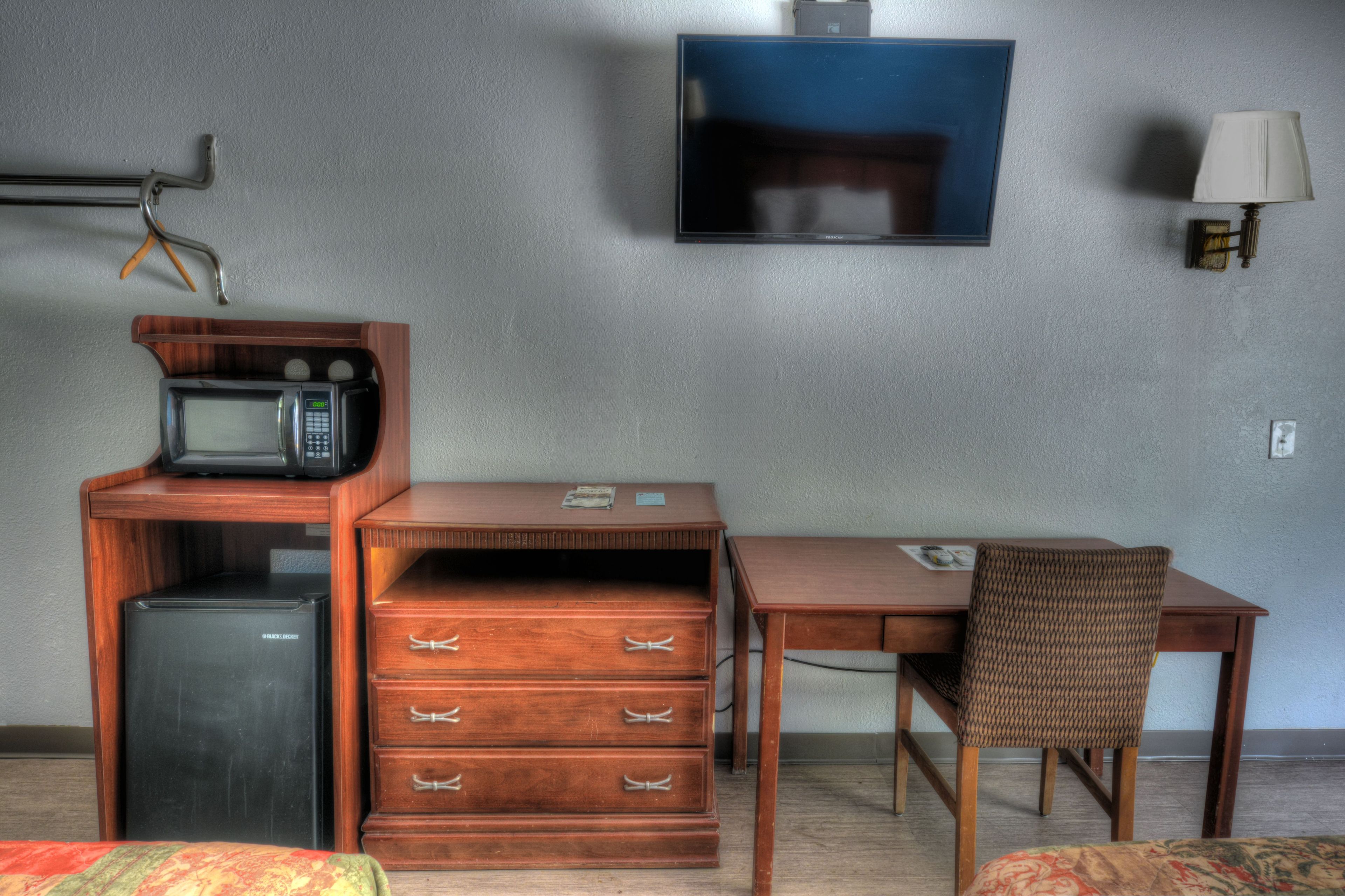 A compact hotel room with a kitchenette, a flat-screen TV, a single bed, and a small desk with a chair.