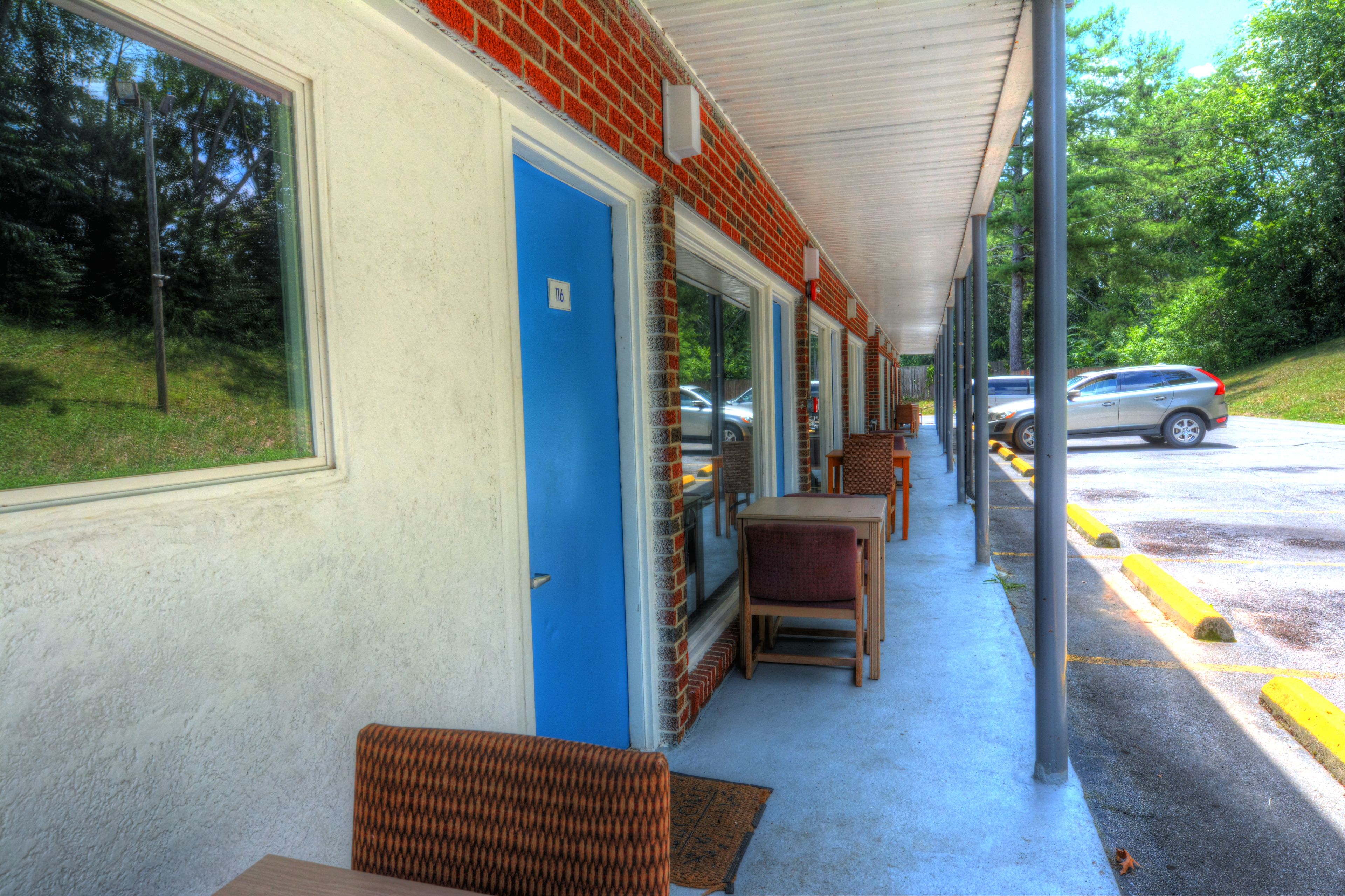 A covered outdoor seating area with tables and chairs, a blue door, and a view of the street with parked cars.