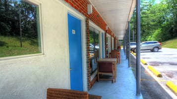 A covered outdoor seating area with tables and chairs, a blue door, and a view of the street with parked cars.
