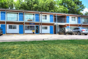 Un motel à la façade bleue et blanche, avec un hall d’entrée bien visible et deux voitures garées devant.