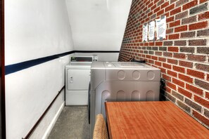 A laundry room with a brick wall, a washing machine, a dryer, and a wooden table. - Volunteer Inn at Church Hill near Kingsport (Church Hill)