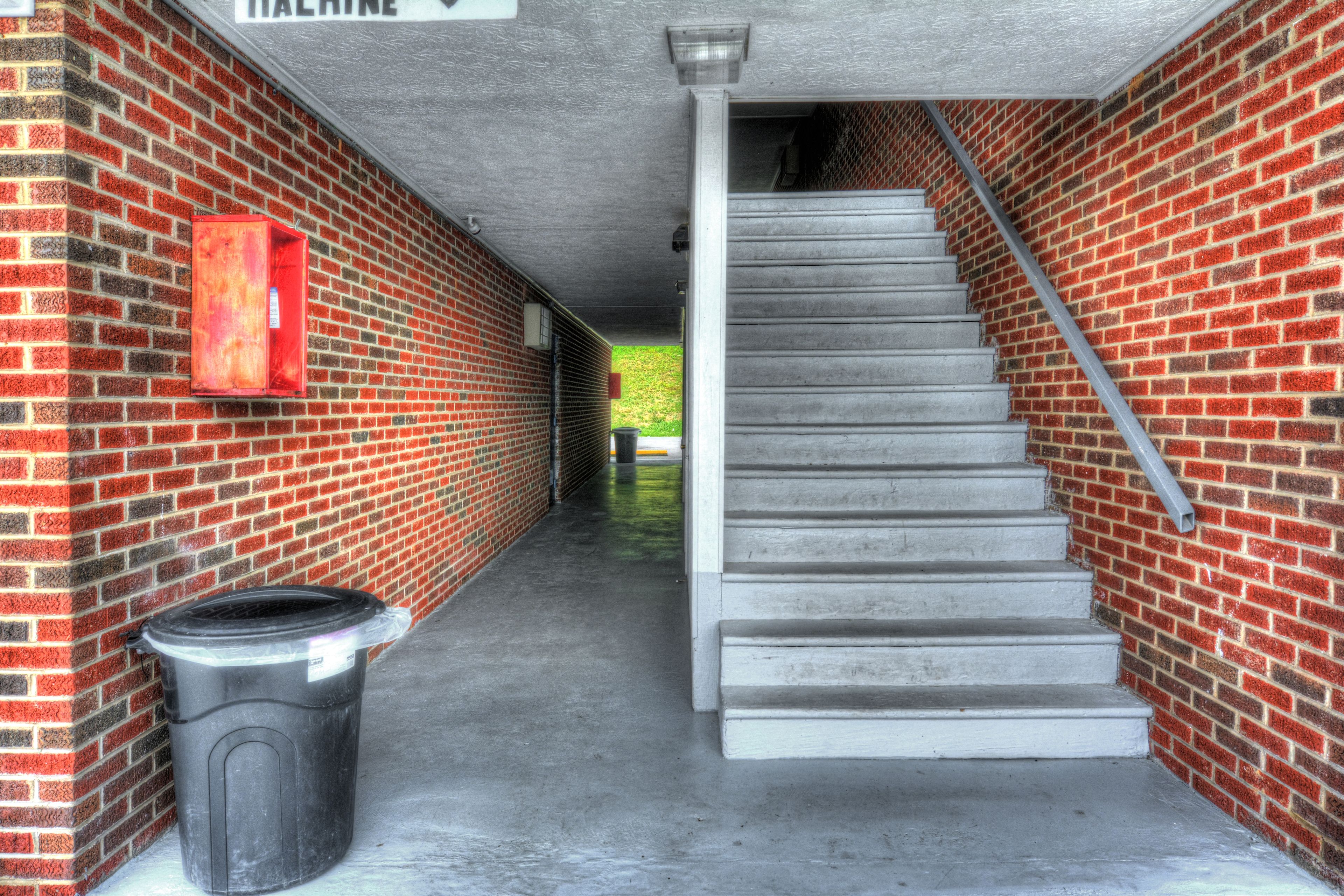 A covered stairway leading to a higher level, flanked by brick walls and a trash bin.