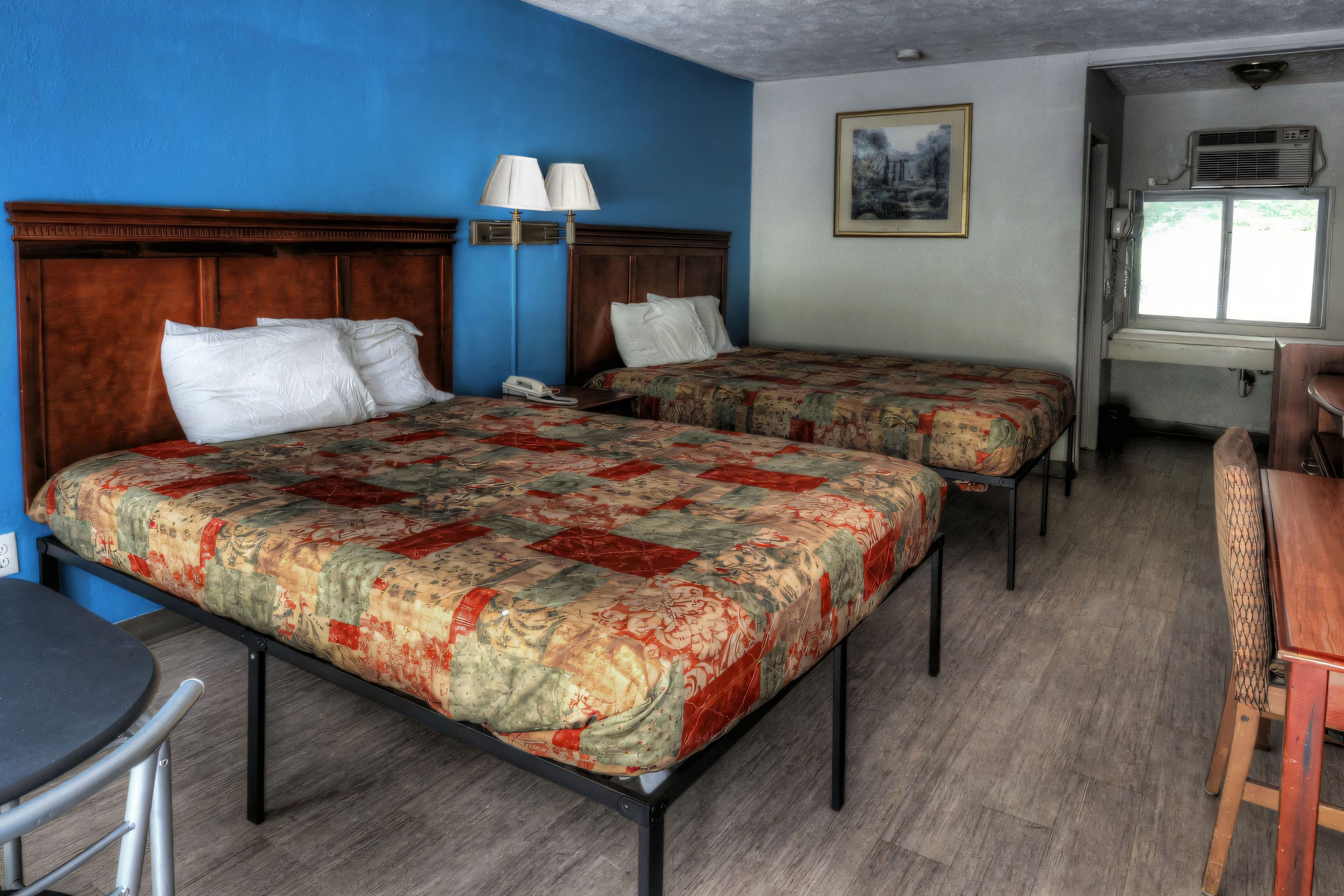 A hotel room with two beds, a desk, a chair, a lamp, and a window.