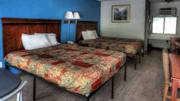 A hotel room with two beds, a desk, a chair, a lamp, and a window.