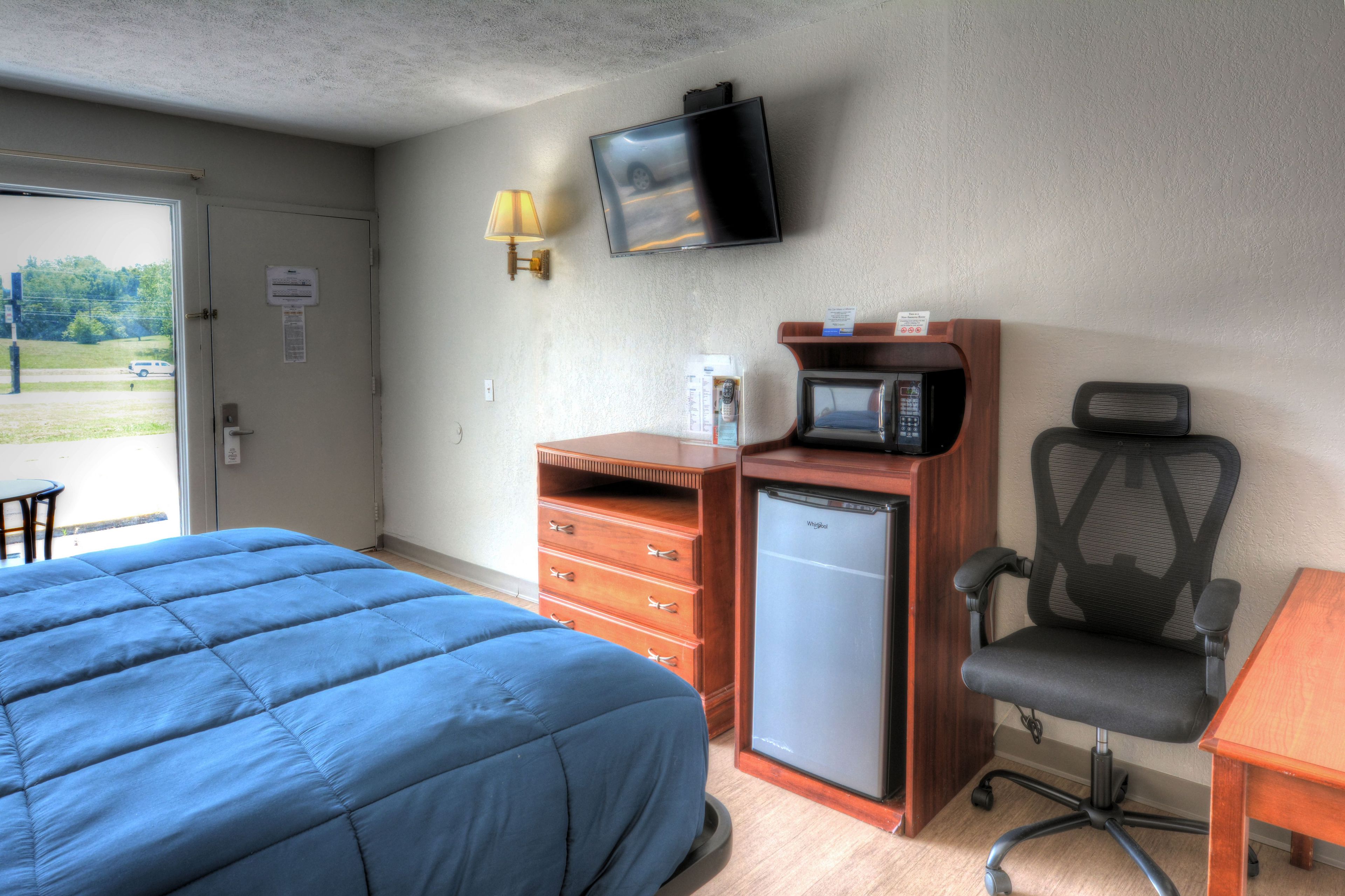 A hotel room with a bed, a desk, a chair, a microwave, a television, and a small refrigerator.
