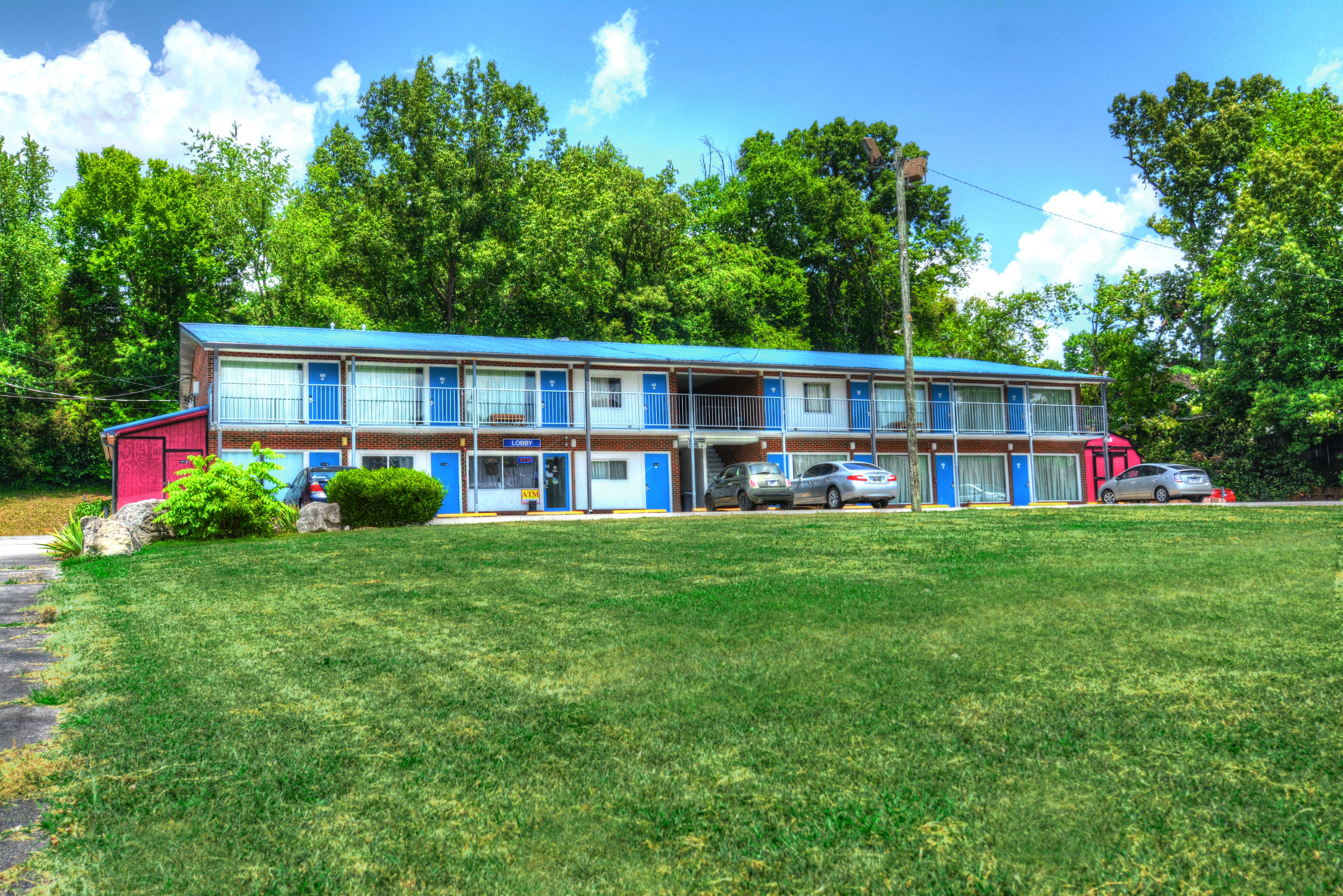 A motel with a blue and red exterior, multiple rooms, and a lawn in front.