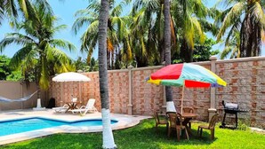 Un patio trasero con piscina, sillas de descanso, una parrilla y palmeras.