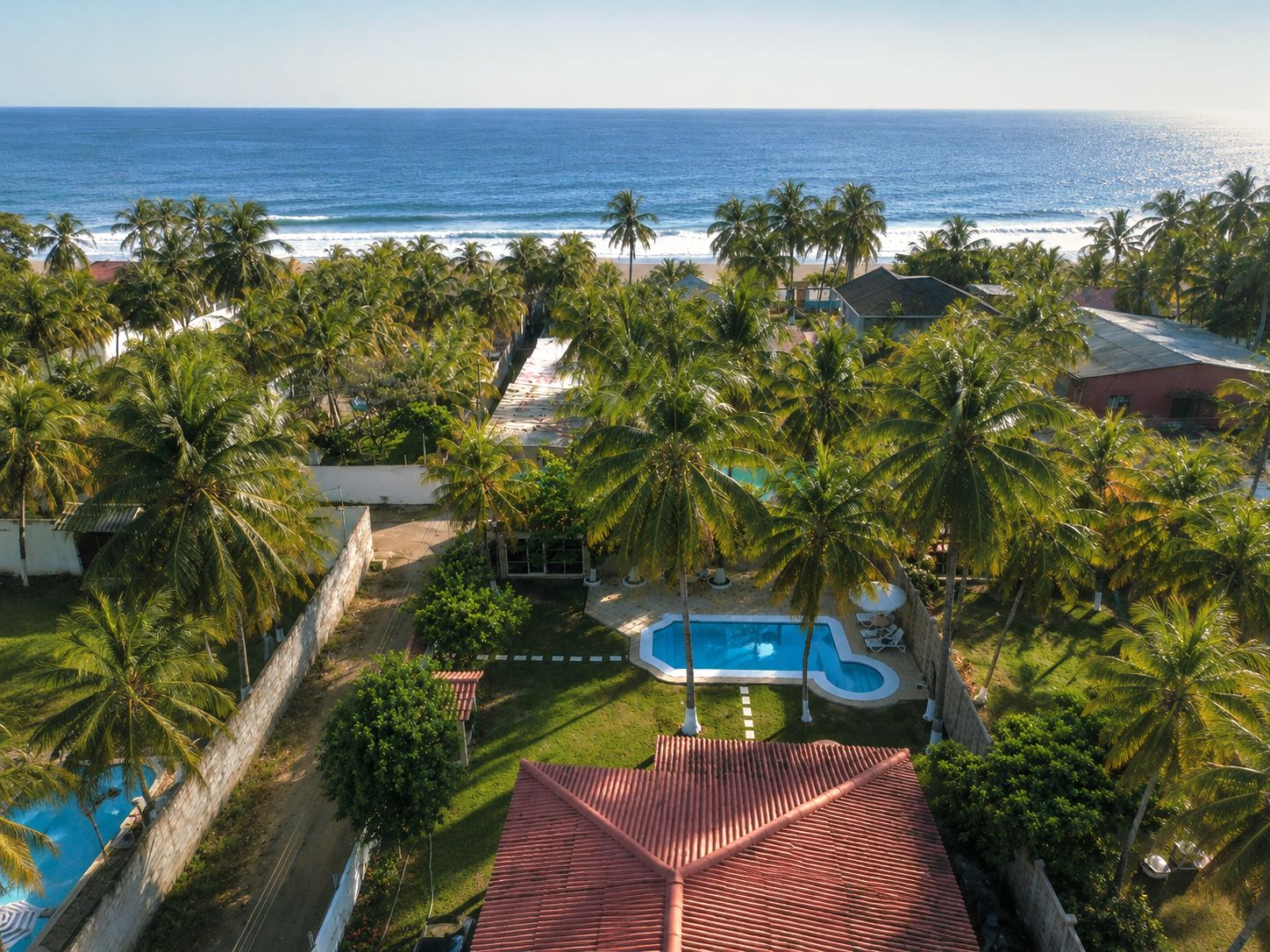Um resort com piscina, palmeiras e vista para o oceano.