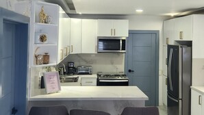 A modern kitchen with a marble countertop, a built-in microwave, a stove, and a refrigerator. There are three bar stools at the counter. - Charming 4-bedroom house with AC and WiFi in fabulous Punta Cana (Punta Cana)
