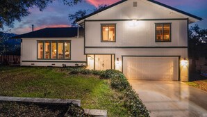 A two-story house with a garage, large windows, and a well-lit exterior at dusk. - Sequoia's Dream: Mountain View, Spa, Heated Floors, Bar, Cinema! Near Yosemite! (Oakhurst)