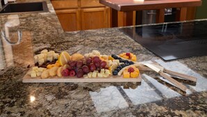 A marble countertop with a wooden cutting board holding various cheeses, fruits, and nuts. - Sequoia's Dream: Mountain View, Spa, Heated Floors, Bar, Cinema! Near Yosemite! (Oakhurst)
