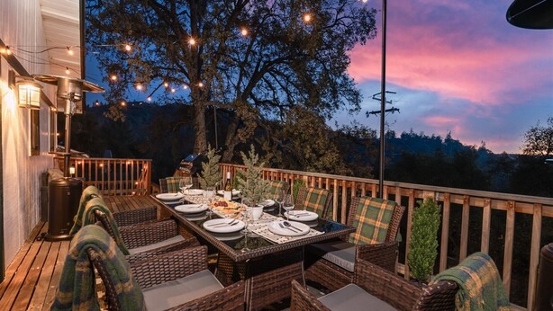 An outdoor dining area with wicker furniture, a table set for four, and string lights. - Sequoia's Dream: Mountain View, Spa, Heated Floors, Bar, Cinema! Near Yosemite! (Oakhurst)
