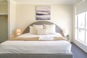 A hotel room with a large bed, two bedside lamps, a painting on the wall, and a window with a view.