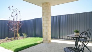 A patio area with a round table and chairs, a small tree, and a metal fence. - StayAU 5BRM Idyllic Retreat for Families in Perth (Baldivis)