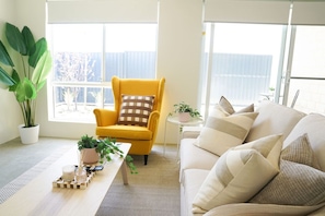 A living room with a yellow armchair, a beige sofa, and a small table with a plant and candles. - StayAU 5BRM Idyllic Retreat for Families in Perth (Baldivis)