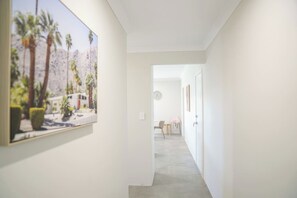 A hallway with a framed picture on the wall, a door at the end, and a chair in the distance.