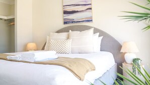 A neatly made bed with white linens and a beige throw blanket, a grey upholstered headboard, and a wall-mounted abstract painting. - StayAU 5BRM Idyllic Retreat for Families in Perth (Baldivis)