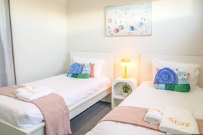 A hotel room with two beds, each with a pillow and a towel. There is a nightstand with a lamp and a small plant. - StayAU 5BRM Idyllic Retreat for Families in Perth (Baldivis)