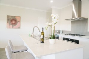 A modern kitchen with a central island, stainless steel appliances, and a potted orchid. - StayAU 5BRM Idyllic Retreat for Families in Perth (Baldivis)
