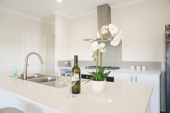 A modern kitchen with a stainless steel sink, wine bottle, and orchid plant on the counter.