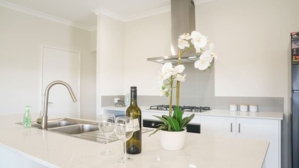 A modern kitchen with a large island, stainless steel appliances, and a potted orchid. - StayAU 5BRM Idyllic Retreat for Families in Perth (Baldivis)