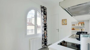 Eine moderne Küche mit weißer Arbeitsplatte, einem Einbauofen und einem Fenster mit dekorativer Vorhang.