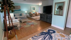 Sala de estar com televisão, mesa de centro, sofá e uma árvore decorativa.