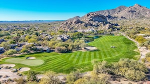 Un parcours de golf avec une chaîne de montagnes en arrière-plan, entouré de bâtiments résidentiels et d’une végétation clairsemée.