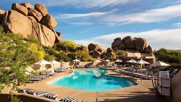 Une piscine entourée de grands rochers et de verdure, avec des chaises longues et des parasols.