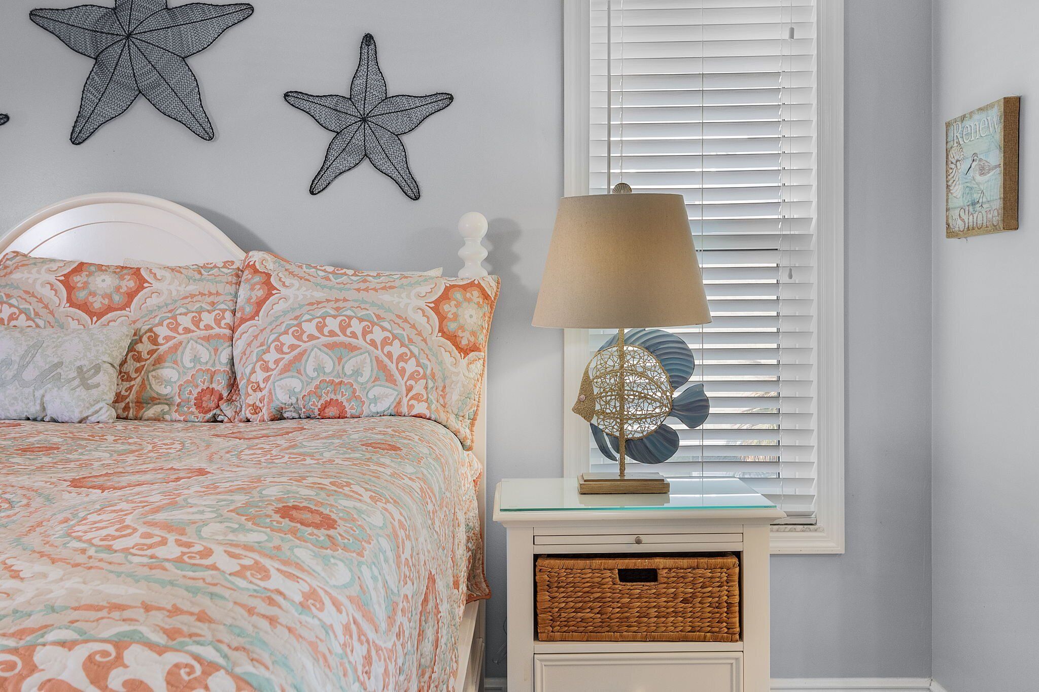 A bedroom with a bed, two starfish wall art, a lamp, and a window with blinds.
