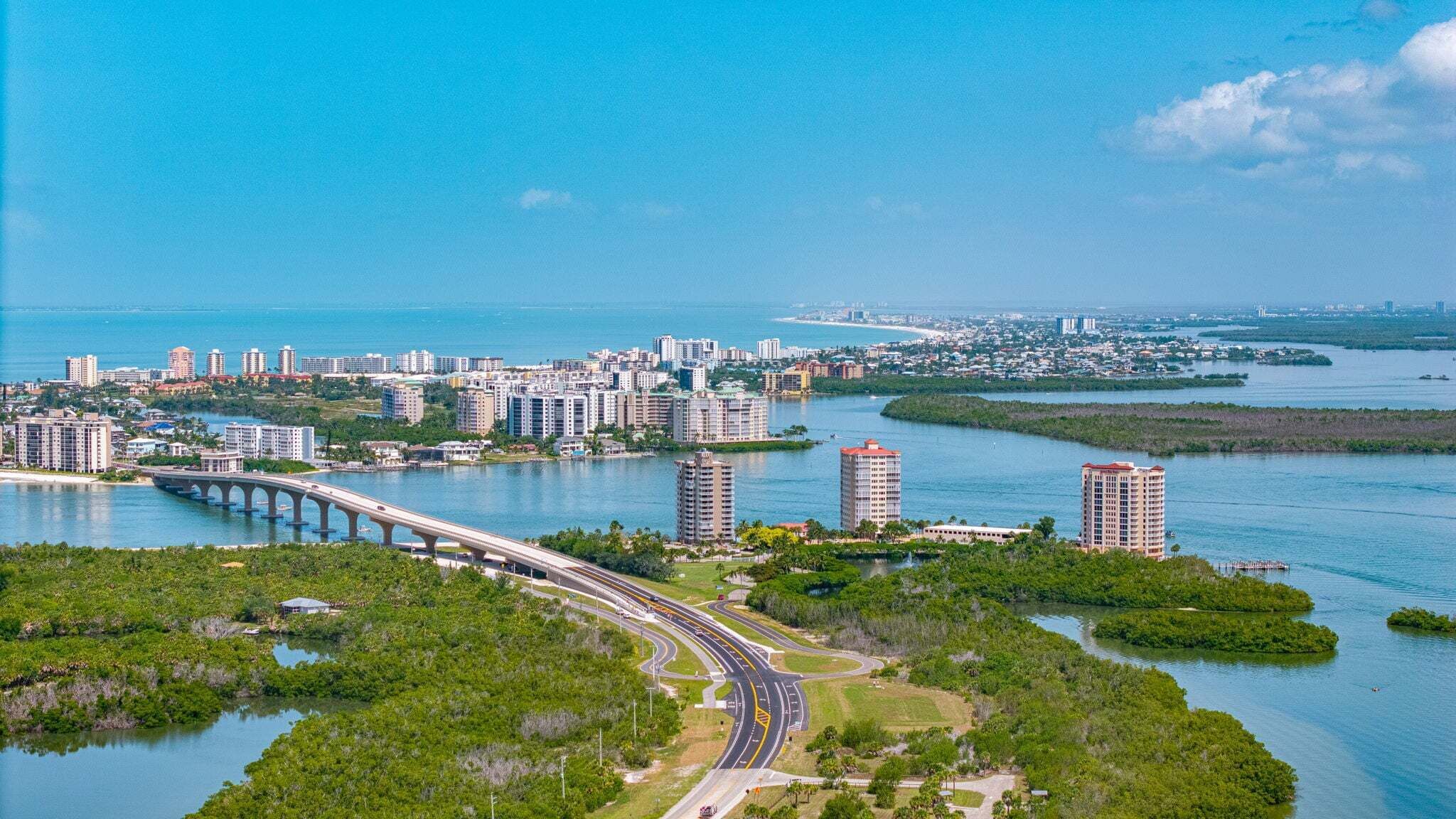 A coastal cityscape with a bridge, dense urban buildings, and a marina.