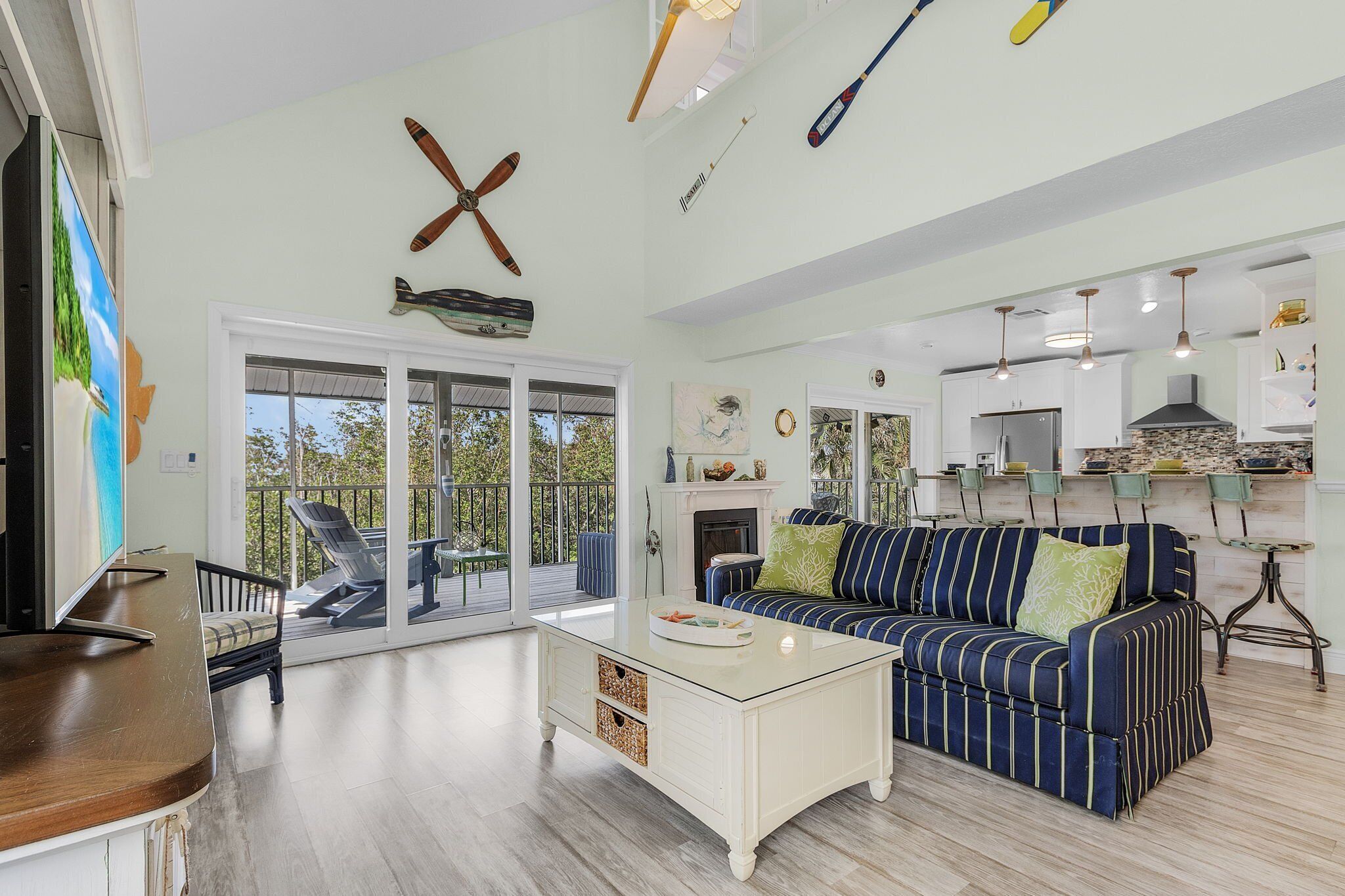 A spacious living room with a large sofa, a coffee table, and a fireplace. There is a balcony with outdoor furniture and a view of the trees.