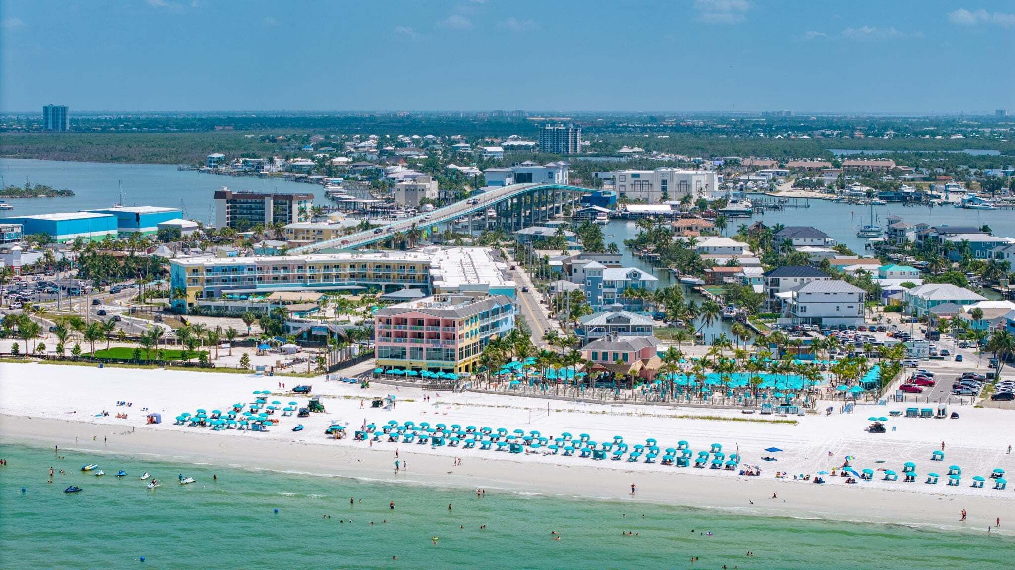 Paisagem costeira com praia, marina e diversos edifícios.