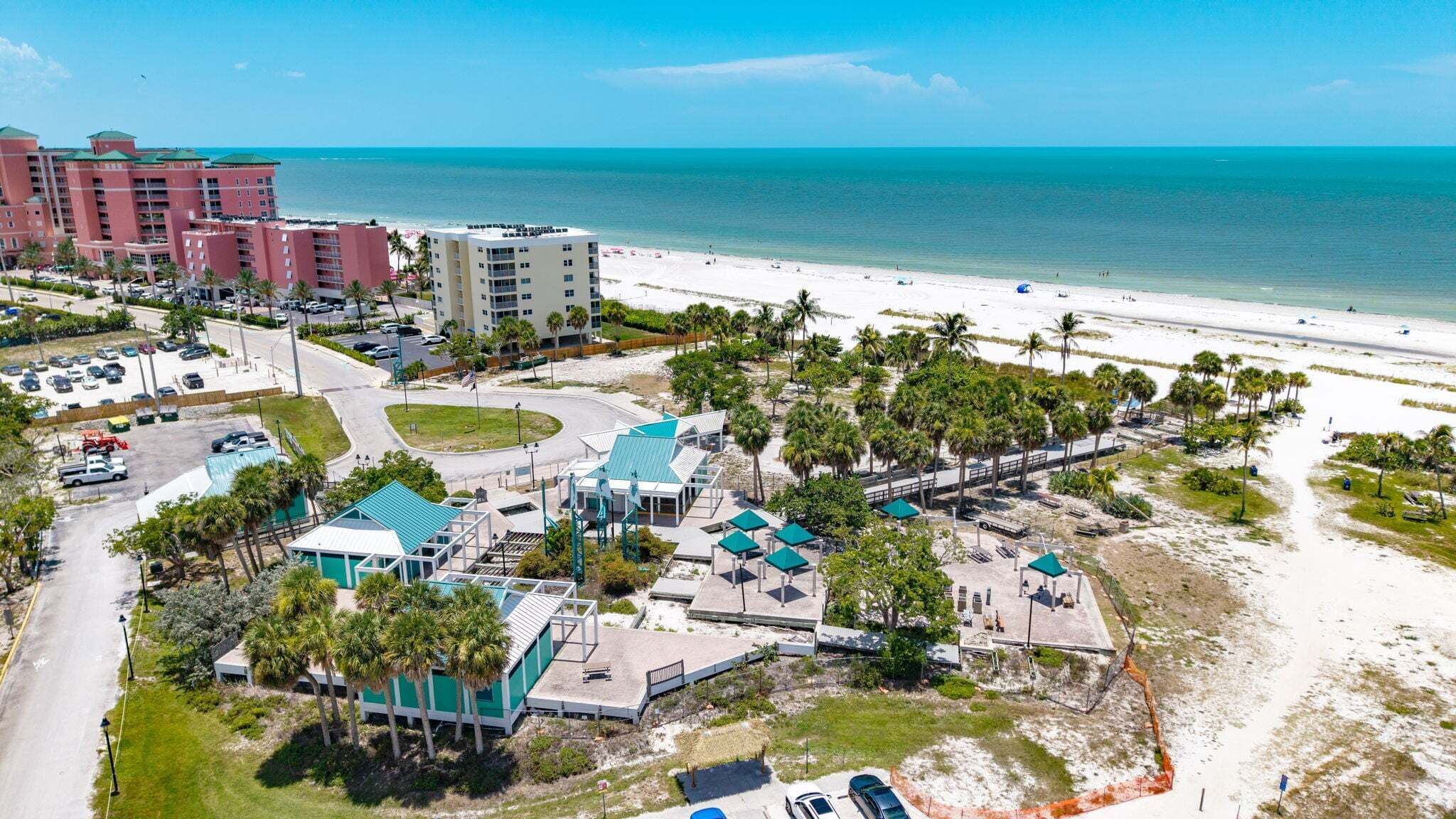 A coastal hotel with multiple buildings, a beach, and a parking area.