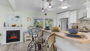 A modern kitchen with a fireplace, bar stools, and a large island with bowls. - Close to Beach, Secluded Pier with Partial Bay Views - Blue Bayou B - Roelens (Fort Myers Beach)
