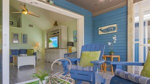 A room with blue walls, a ceiling fan, a television, a sofa, and a chair with a green pillow. - Close to Beach, Secluded Pier with Partial Bay Views - Blue Bayou B - Roelens (Fort Myers Beach)