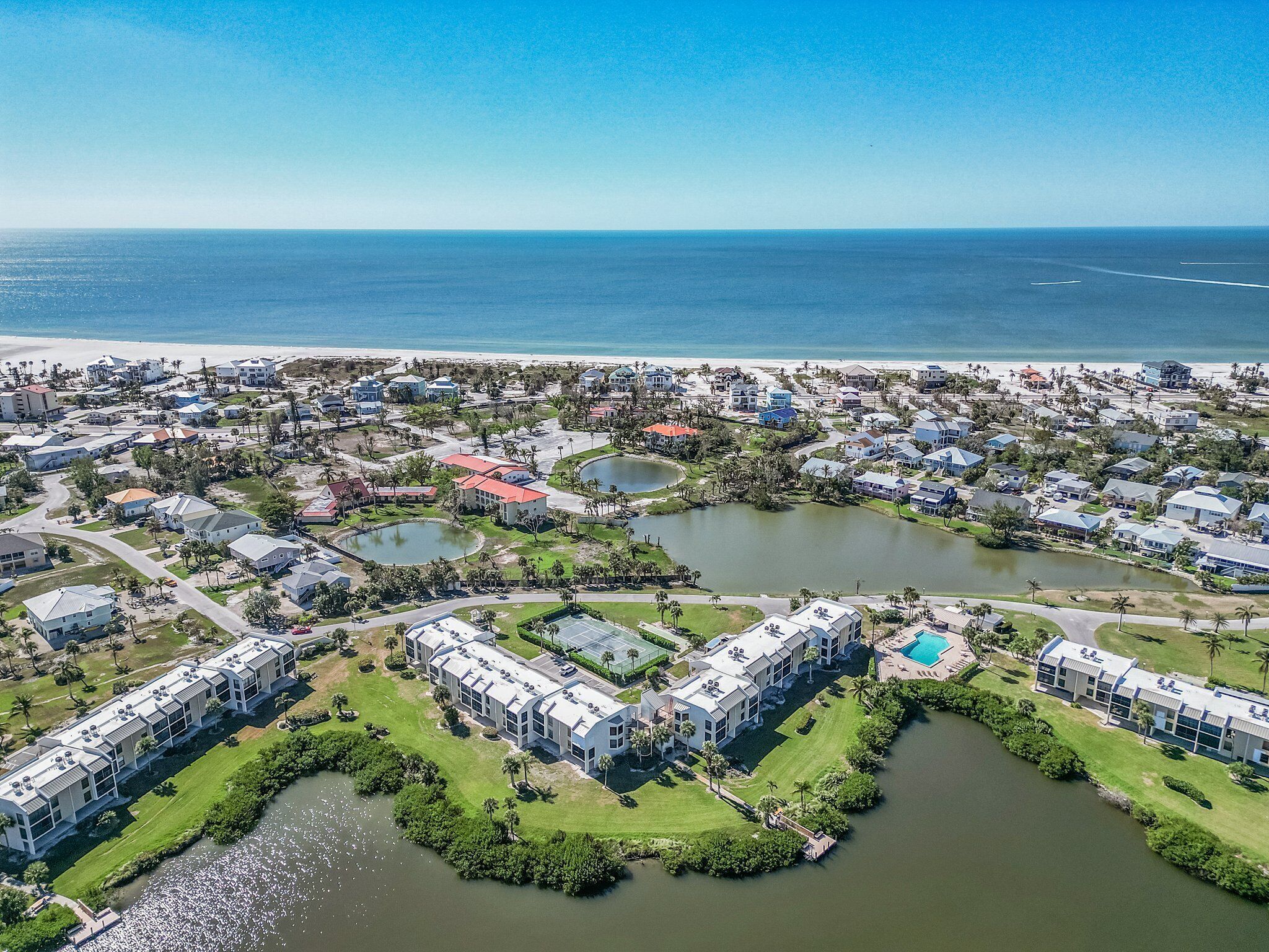An aerial view of a coastal residential area with houses, a beach, and a lake.