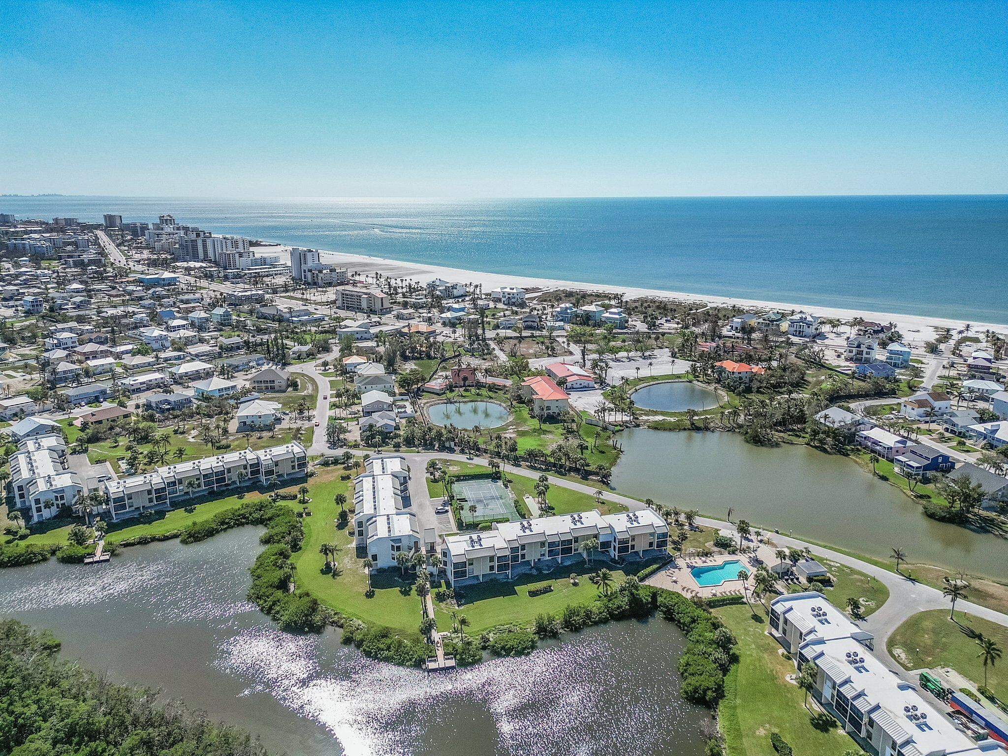 Vista aérea de una zona residencial costera con un puerto deportivo, una playa y una gran masa de agua.