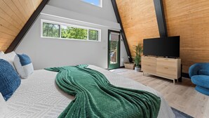 A bedroom with a bed, a television, a dresser, and a window with a view of trees. - LEDCabin, See the Stars, w/private Sauna, Hot Tub, on Creekfront (Omaha)