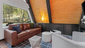 A modern living room with a brown leather sofa, a white round coffee table, and a fireplace. - LEDCabin, See the Stars, w/private Sauna, Hot Tub, on Creekfront (Omaha)